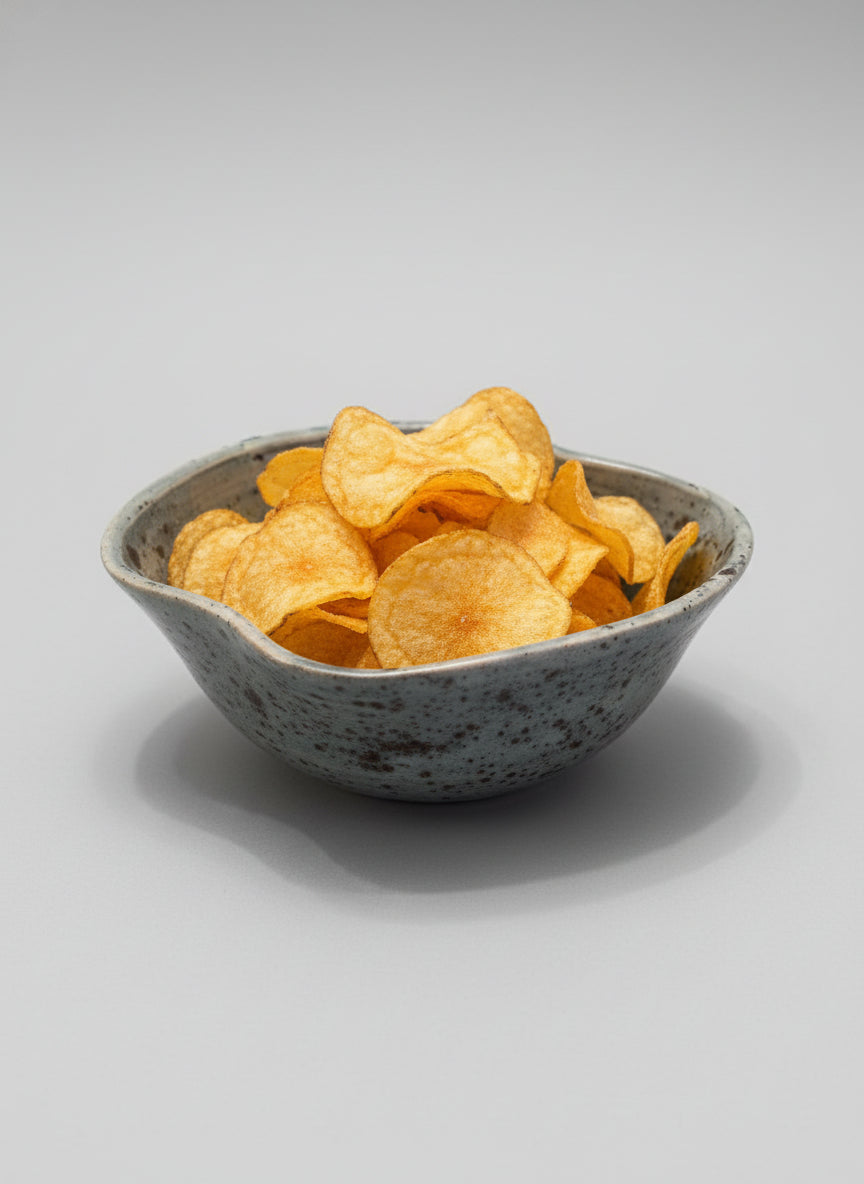 Speckled ceramic bowl on a white surface full of crisps