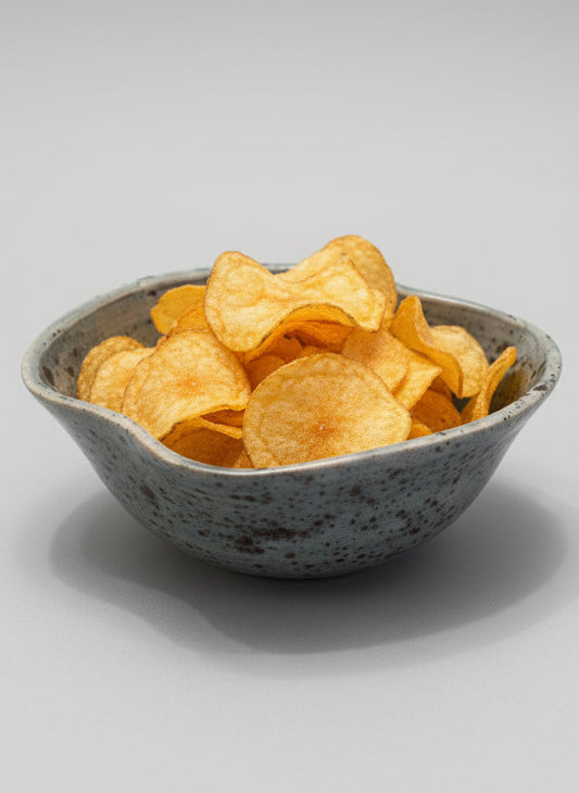 Speckled ceramic bowl on a white surface full of crisps